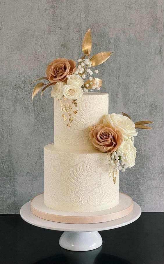 A two-tier cream wedding cake finished with blush roses and gold leaf